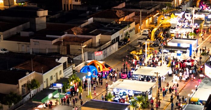 Vista aérea noturna de rua com estandes iluminados e público circulando em feira